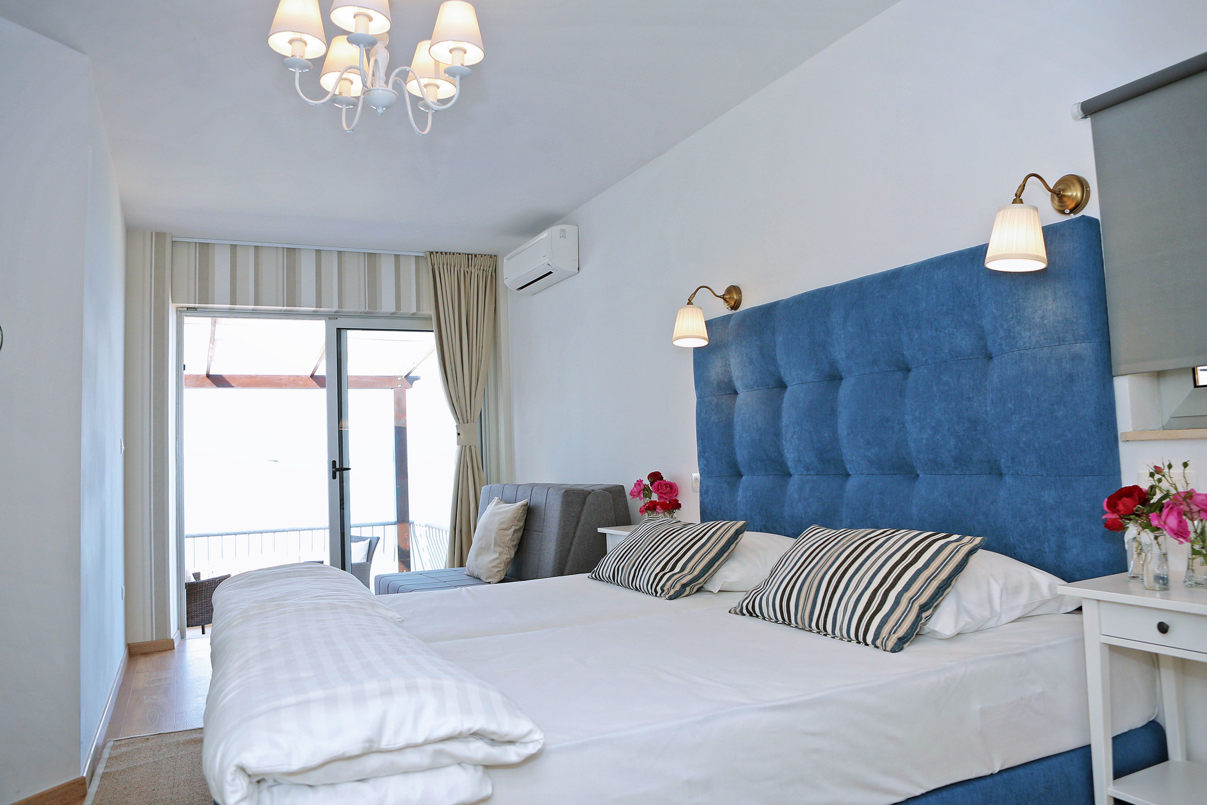A bedroom with a large bed, a blue headboard, bedside lamps, and a view of the balcony.