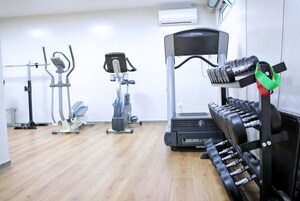 Uma academia com diversos equipamentos de exercício, incluindo esteira, elíptico e suporte para pesos.
