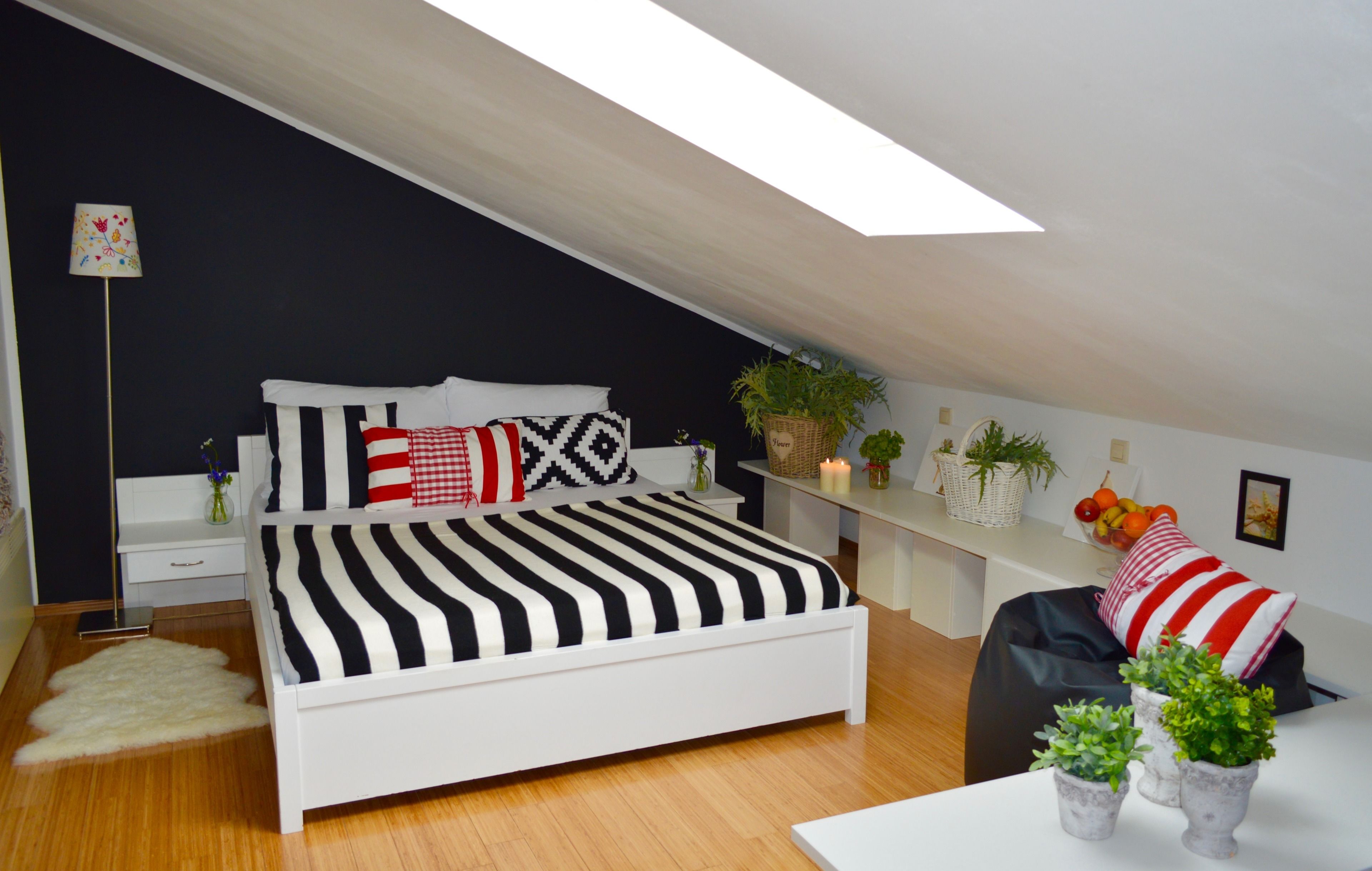 A modern bedroom with a sloped ceiling, a white bed with striped bedding, a bedside table with a lamp, and a small plant on the nightstand.