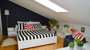 Ein modernes Schlafzimmer mit schrägem Dach, einem weißen Bett mit gestreifter Bettwäsche, einem Nachttisch mit Lampe und einer kleinen Pflanze auf dem Beistelltisch.