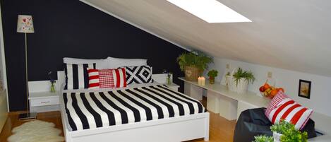 A modern bedroom with a sloped ceiling, a white bed with striped bedding, a bedside table with a lamp, and a small plant on the nightstand.
