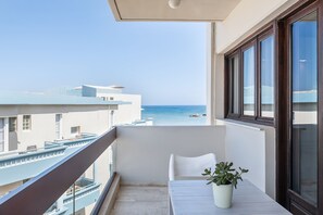 A balcony with a potted plant, a white table, and a view of the sea. - Magia Apartments (Chania)