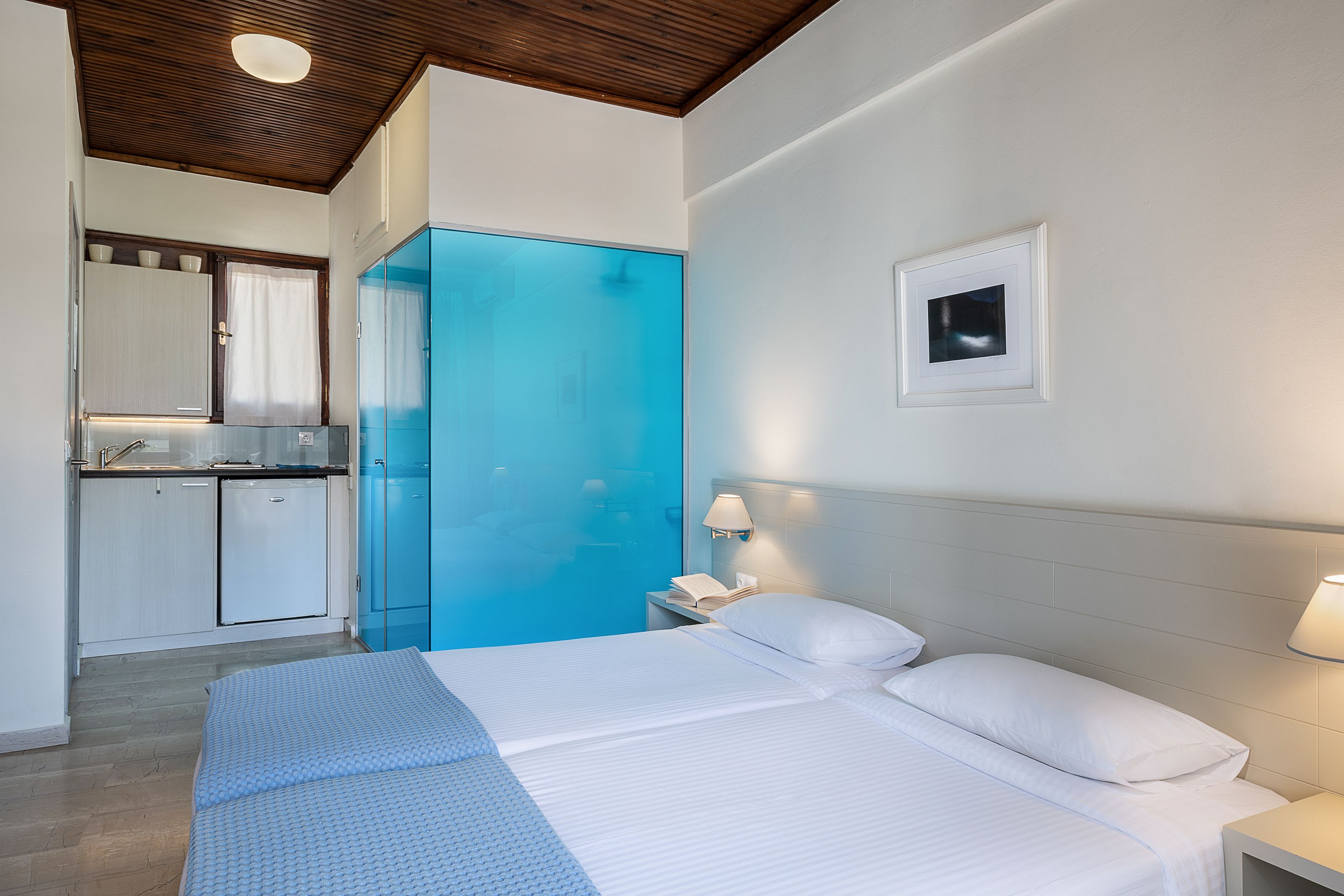 A hotel room with a bed, bedside table, and a small kitchenette.