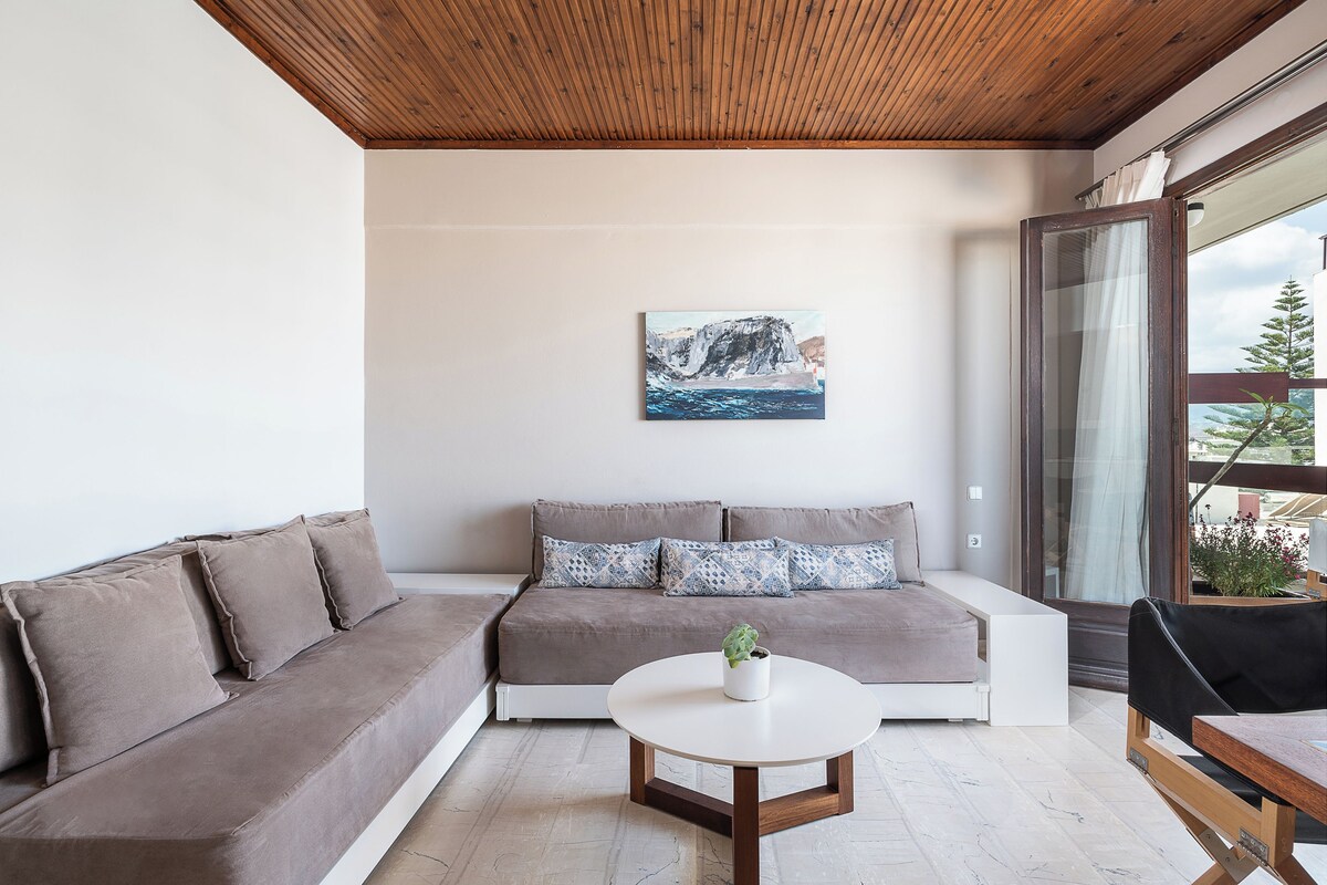 Una sala de estar moderna con un sofá marrón, una mesa de centro blanca y un cuadro de un paisaje montañoso.