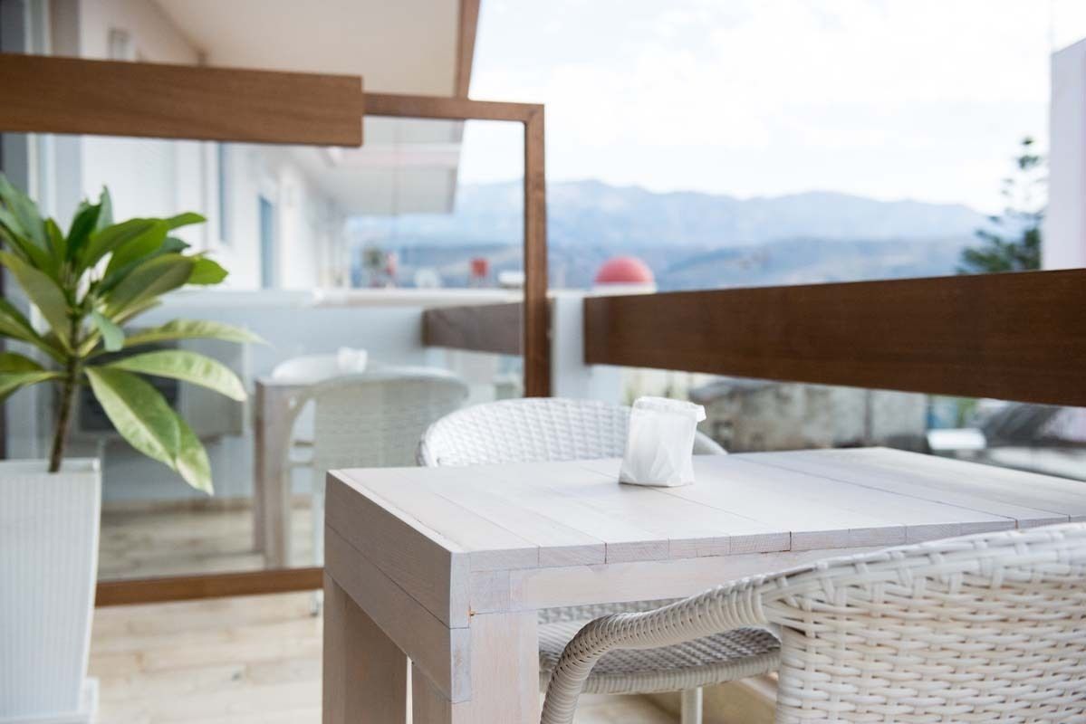 A balcony with a wooden table and wicker chairs, overlooking a mountainous landscape.