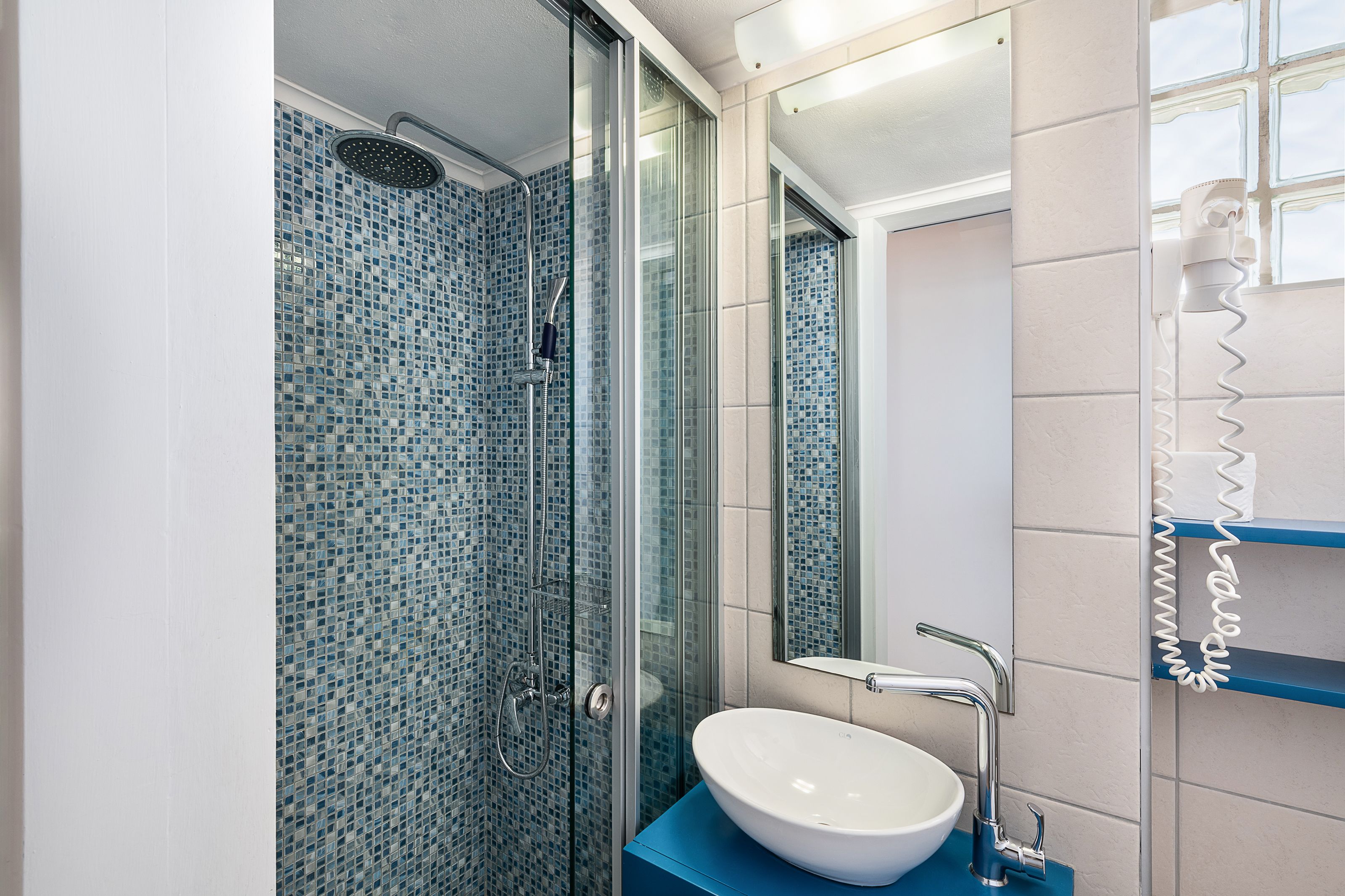 A bathroom with a glass-enclosed shower, a white sink, and a mirror.