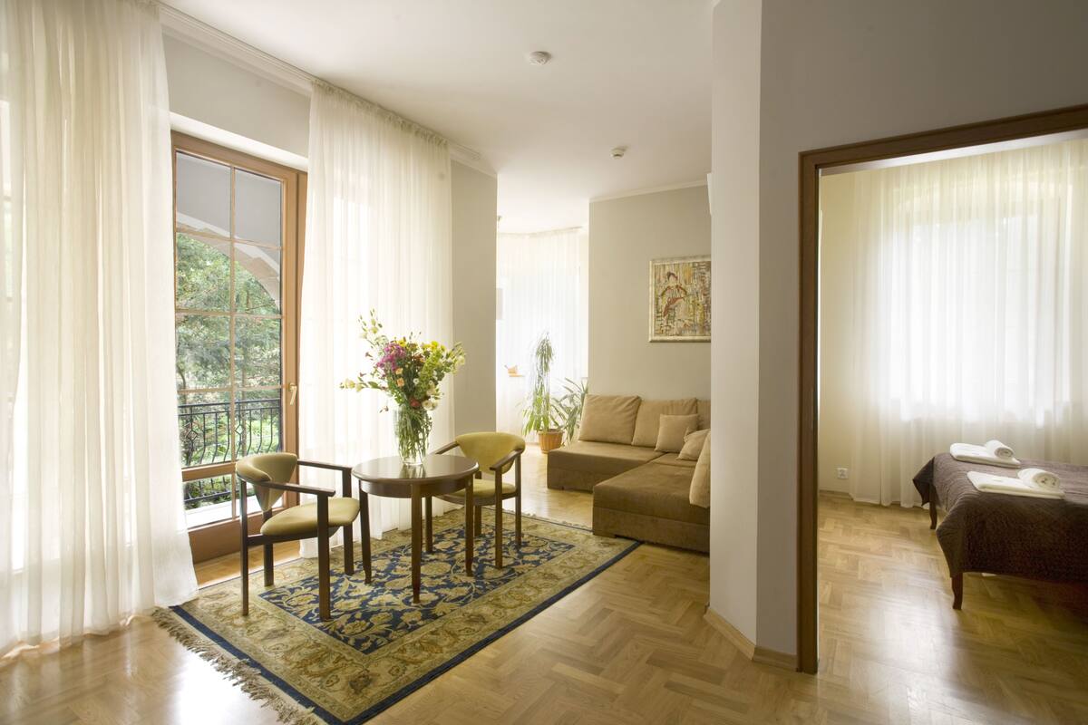 Amplia sala de estar con piso de madera, un sofá, una mesa de comedor con sillas y un balcón con cortinas.