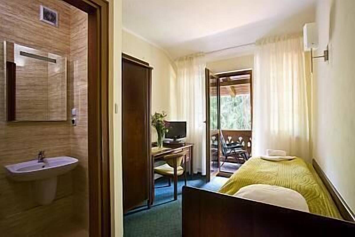 Habitación de hotel con cama, escritorio con computadora, lavamanos y ventana con cortinas.