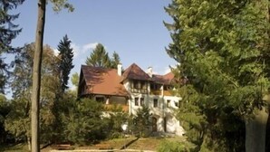 Ein großes Haus mit rotem Dach, umgeben von üppiger Vegetation und Bäumen.