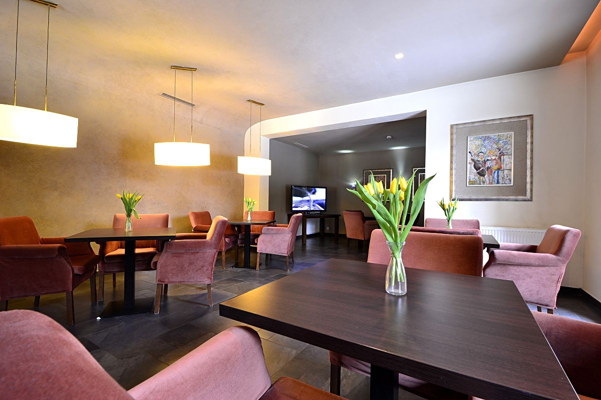 A modern dining area with dark wood tables and orange chairs, a vase with flowers, and a television in the background.
