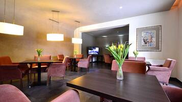 A modern dining area with dark wood tables and orange chairs, a vase with flowers, and a television in the background.