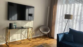 Una sala de estar moderna con un televisor de pantalla plana, una mesa de centro de vidrio, un sofá azul y una lámpara de pie.