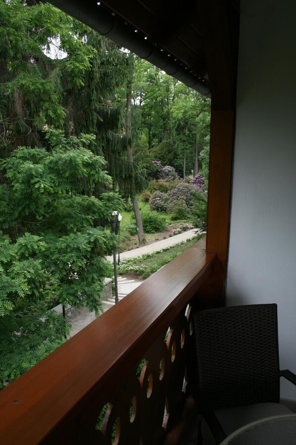 A balcony with a view of a garden, a chair, and a street lamp.