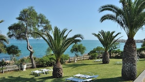 A grassy outdoor area with palm trees and white lounge chairs facing a body of water.