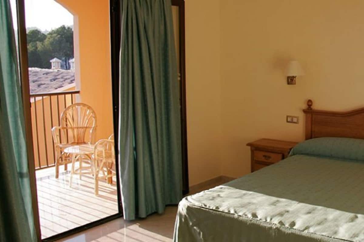 Une chambre avec un lit en bois, deux tables de chevet et une vue sur un balcon équipé de chaises.