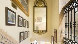 Una imponente escalera con barandales ornamentados, obras de arte en las paredes y un espejo grande en la parte superior.