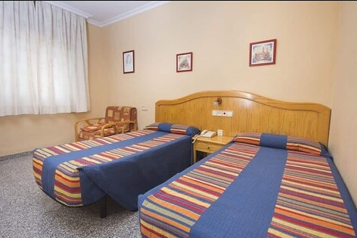 Hotellihuone, jossa on kaksi erillistä sänkyä, puinen pääty ja pieni pöytä sekä tuoli.