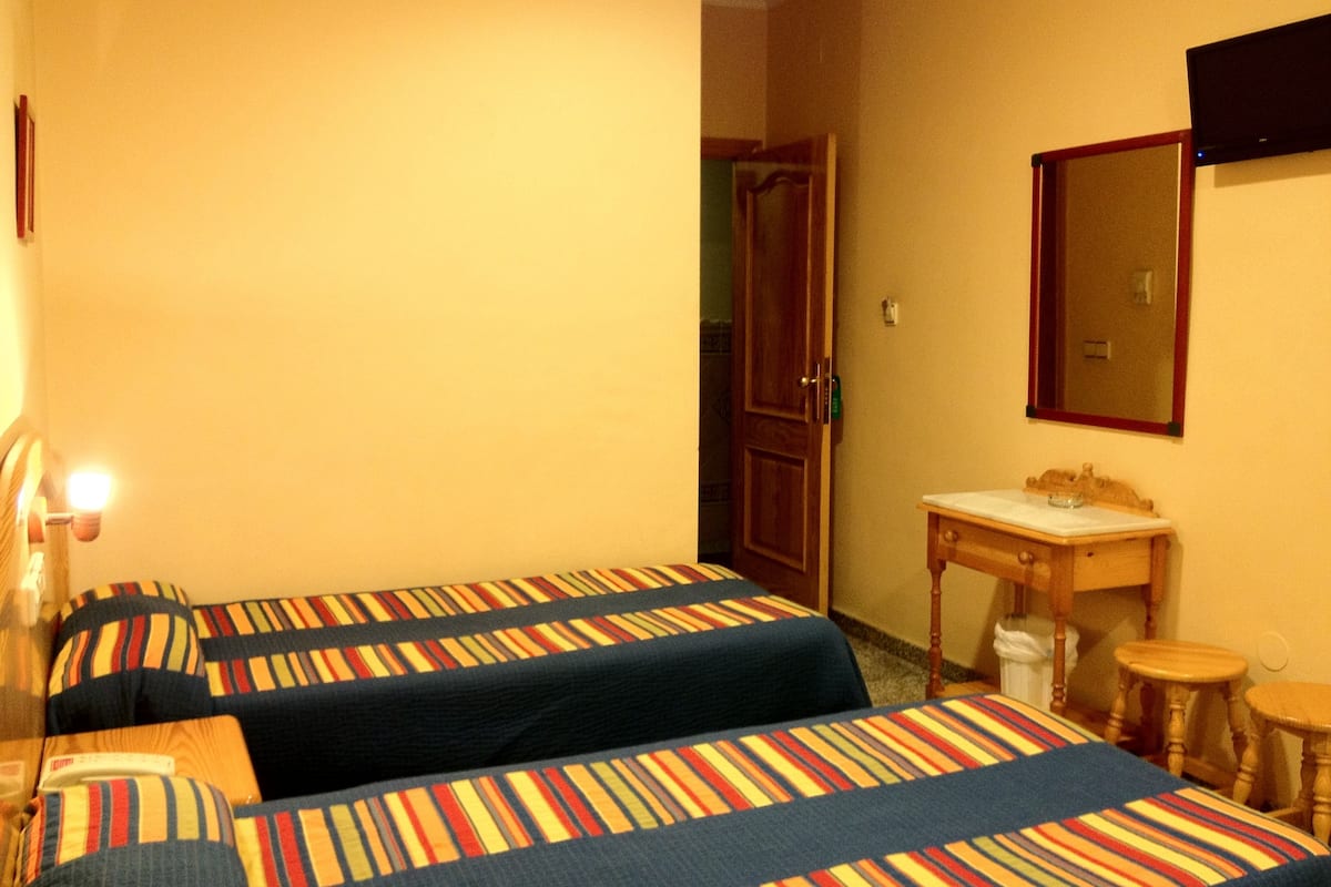 Hotellihuone, jossa on kaksi sänkyä, puinen yöpöytä, pieni pöytä ja peili.