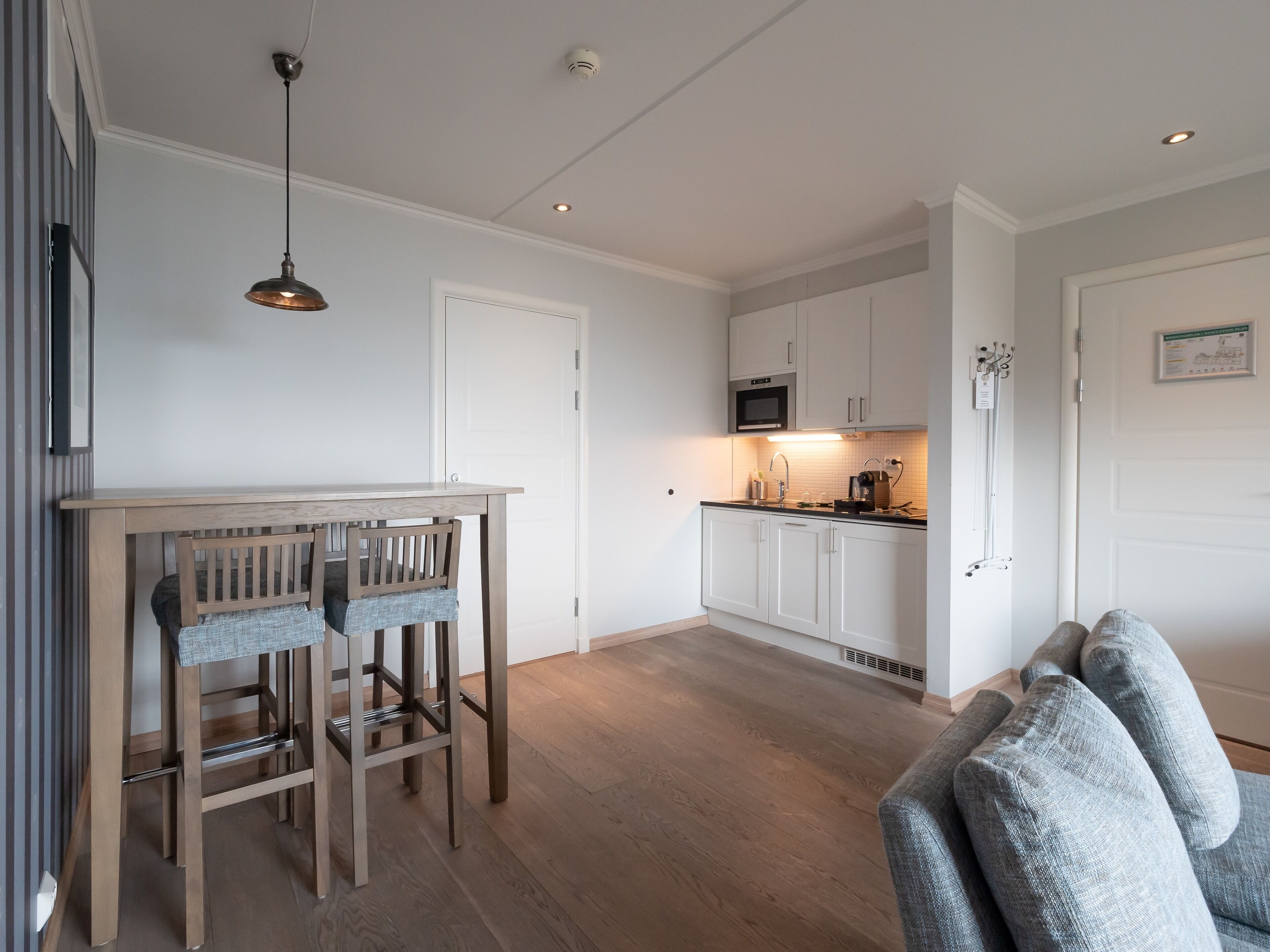 Une cuisine moderne avec des meubles blancs, une table à manger en bois et un micro-ondes encastré.