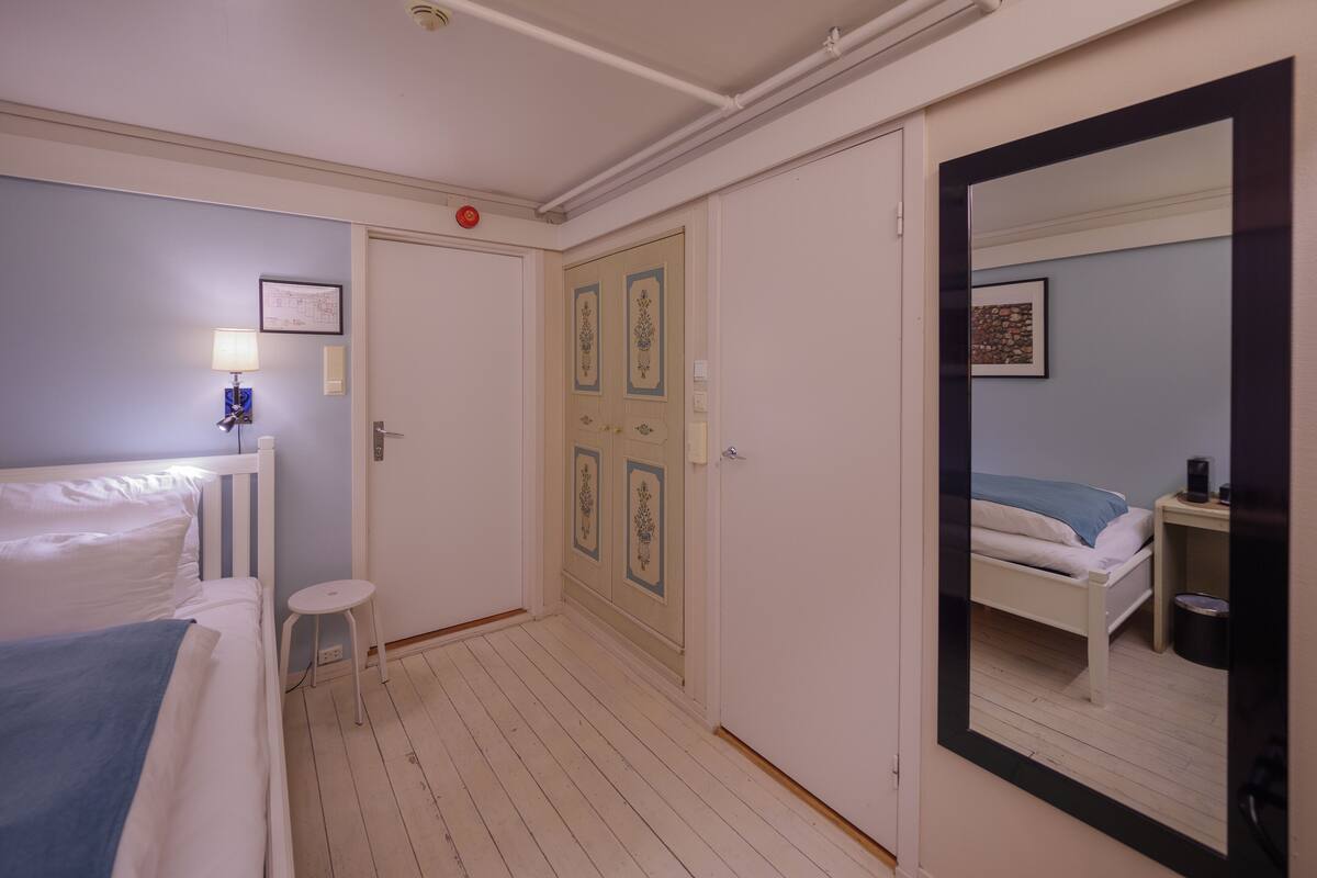 Una habitación de hotel con cama, una mesita, un espejo y una puerta con paneles decorativos.