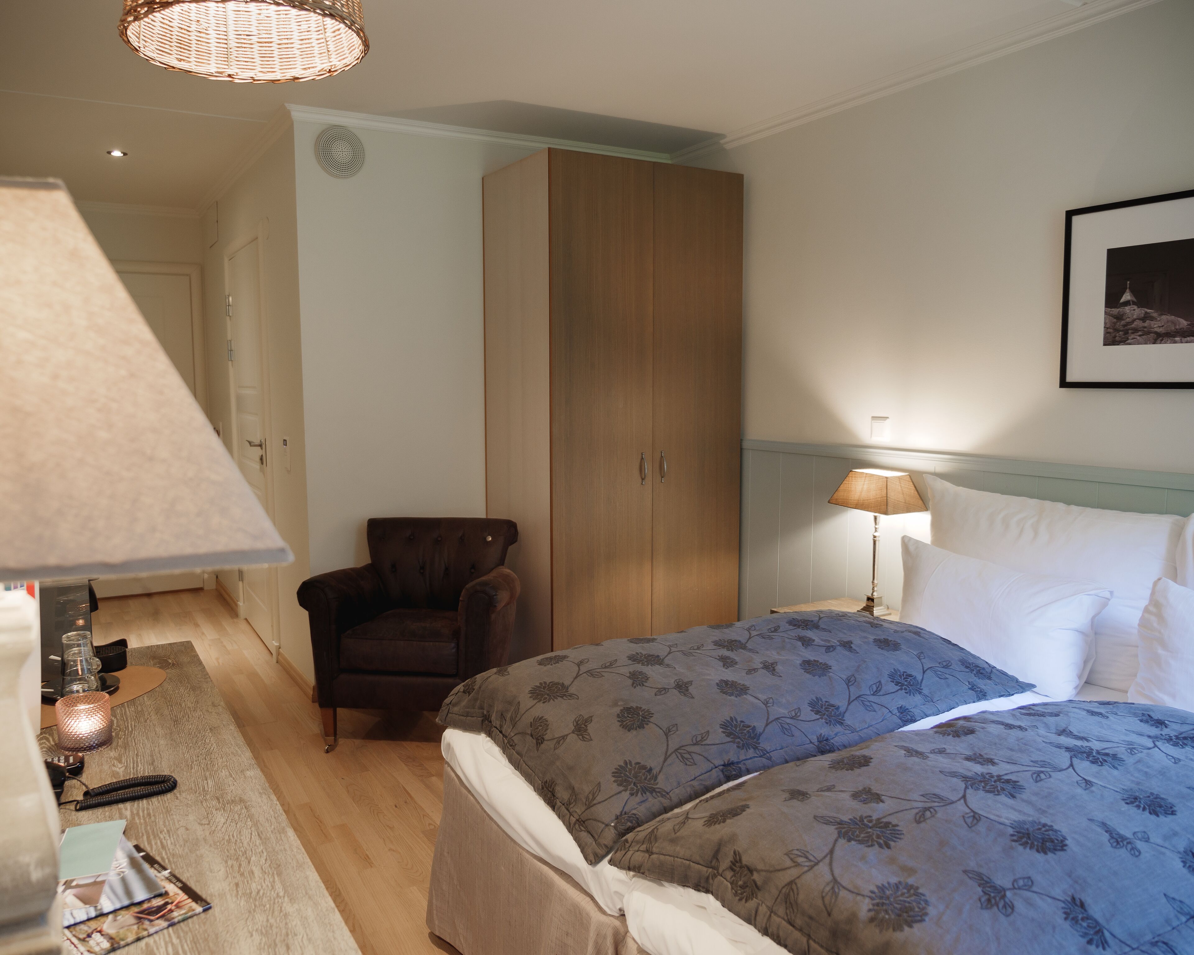 Een slaapkamer met twee bedden, een garderobe, een stoel, een lamp en een lijst met een afbeelding aan de muur.