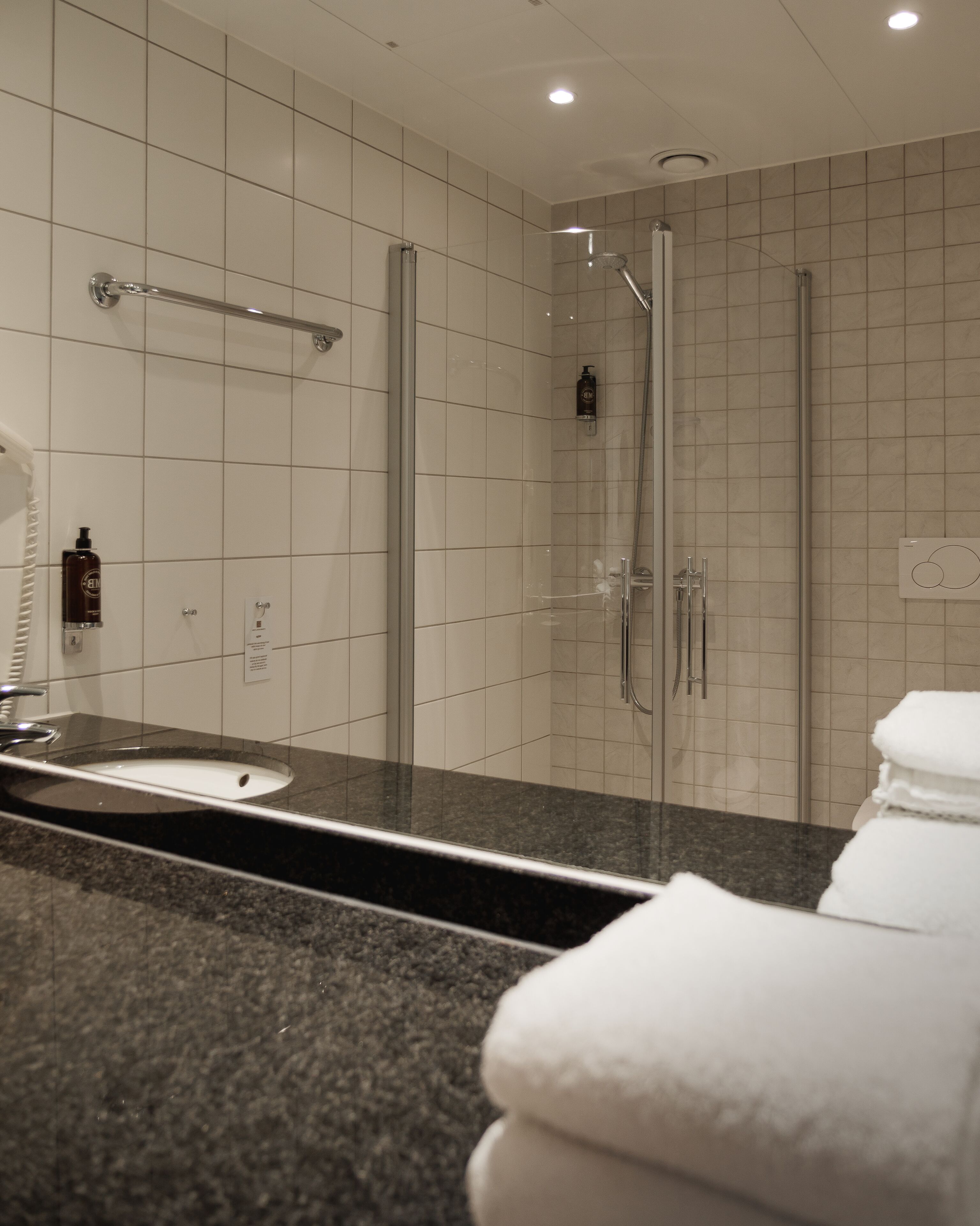 Une salle de bain moderne avec une douche à parois de verre, un comptoir en granit et un lavabo blanc.