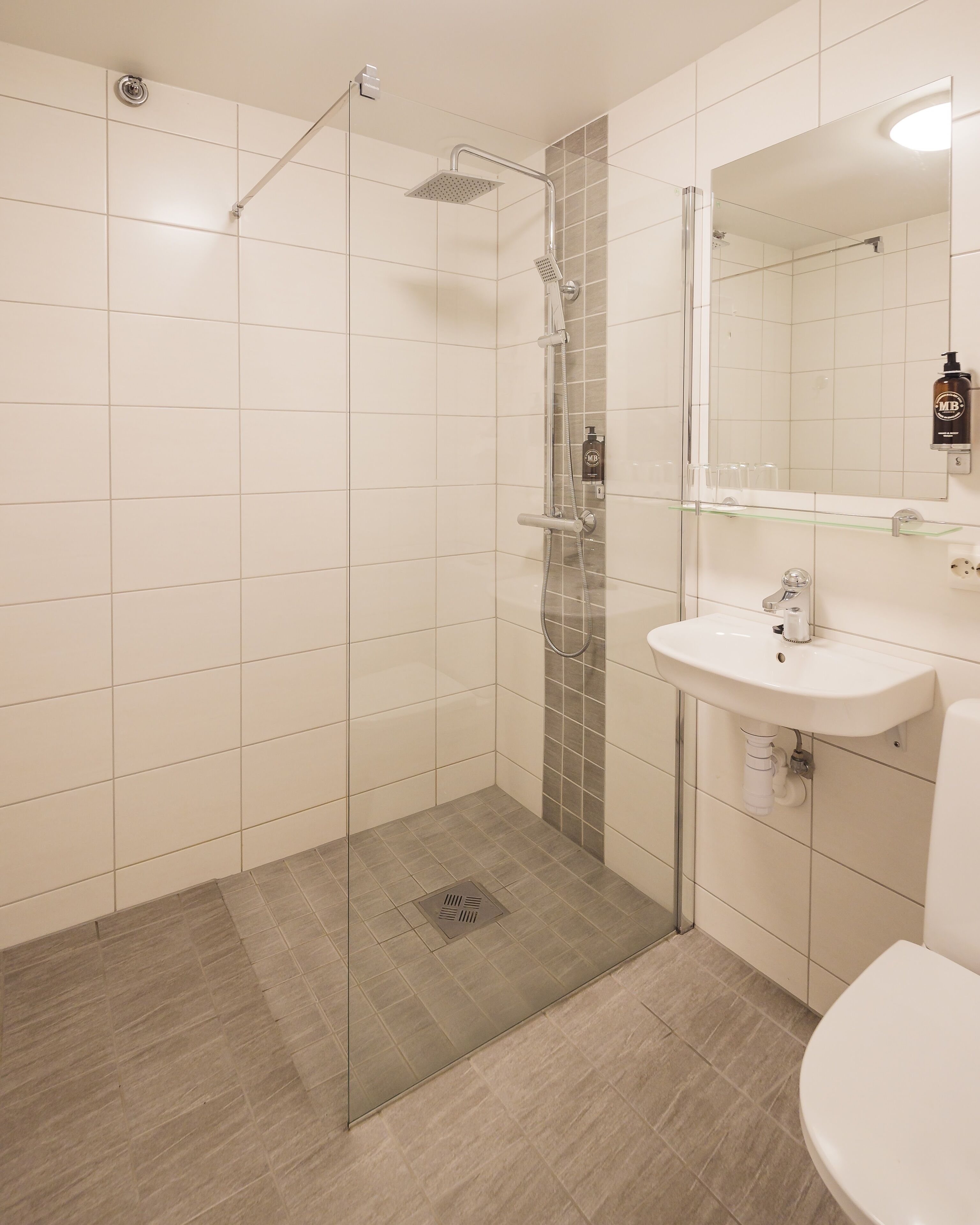 Un baño moderno con ducha de vidrio, lavamanos blanco y espejo sobre el lavamanos.