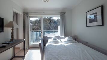 A hotel room with a bed, a desk with a lamp, a television, and a balcony with curtains.