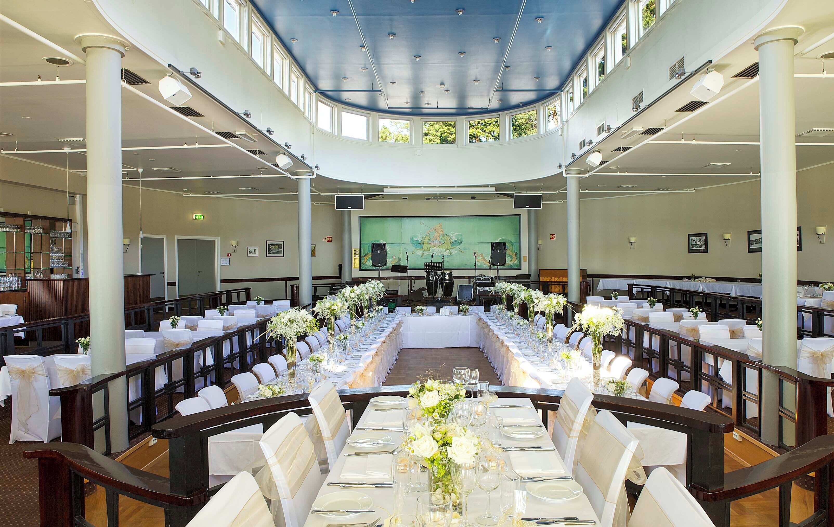 Une salle de banquet avec une longue table dressée pour un événement formel, entourée de chaises recouvertes de housses blanches.