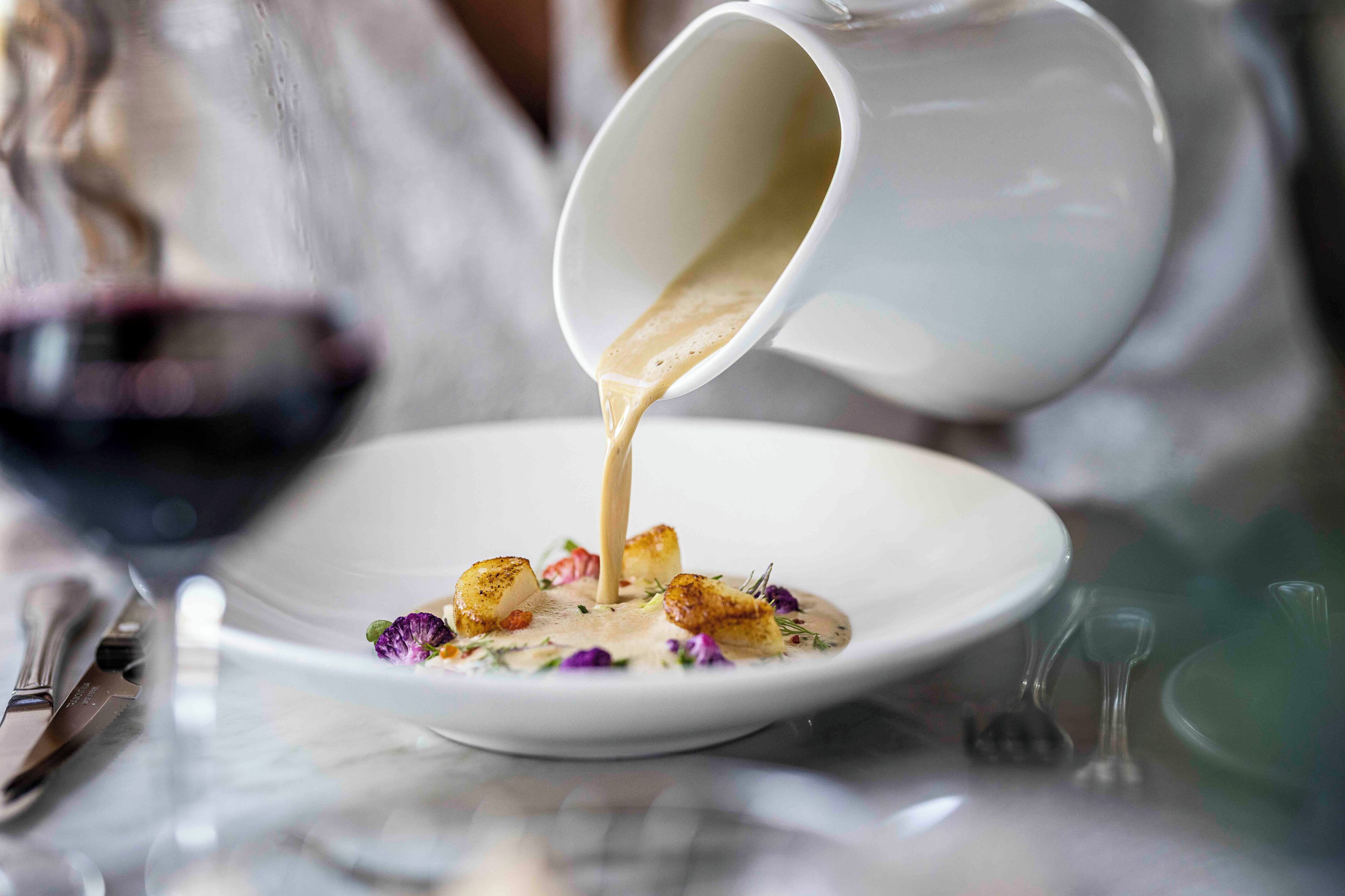 Un plato blanco con salsa cremosa que se vierte desde una jarra blanca.