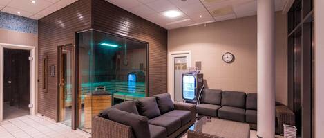 A modern indoor space with a dark brown sofa, a wicker ottoman, and a glass-enclosed area with a blue light.