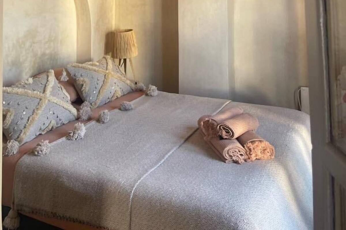 A bedroom with a bed, a hanging light fixture, and a wall-mounted lamp.