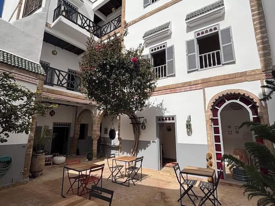 A courtyard with a wooden table and chairs, surrounded by a white building with balconies and windows.