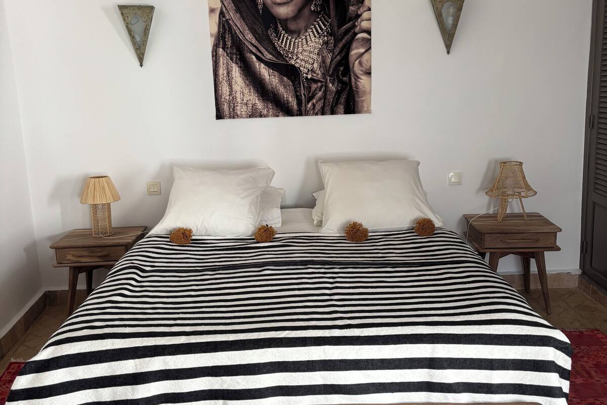 A bed with a striped bedspread, two nightstands with lamps, and a wall-mounted tapestry.