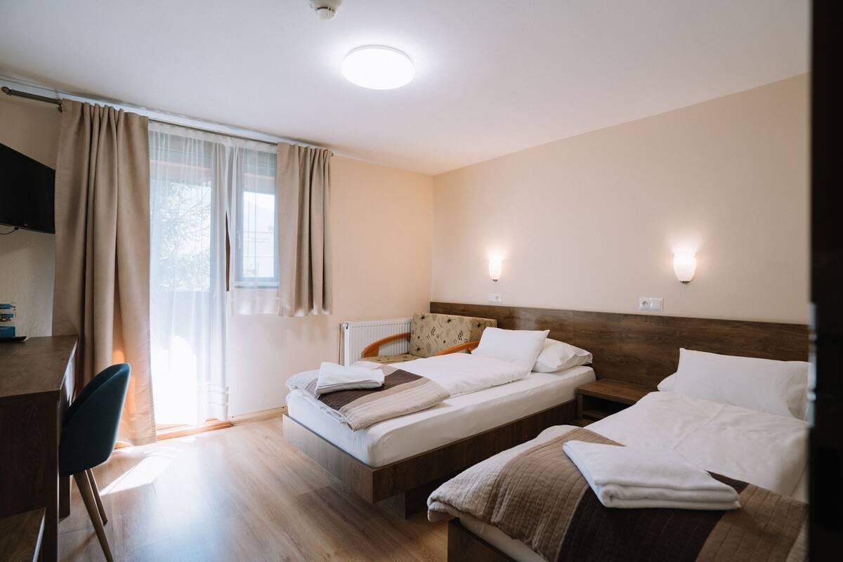 A hotel room with two beds, a desk, a chair, and a window with curtains.
