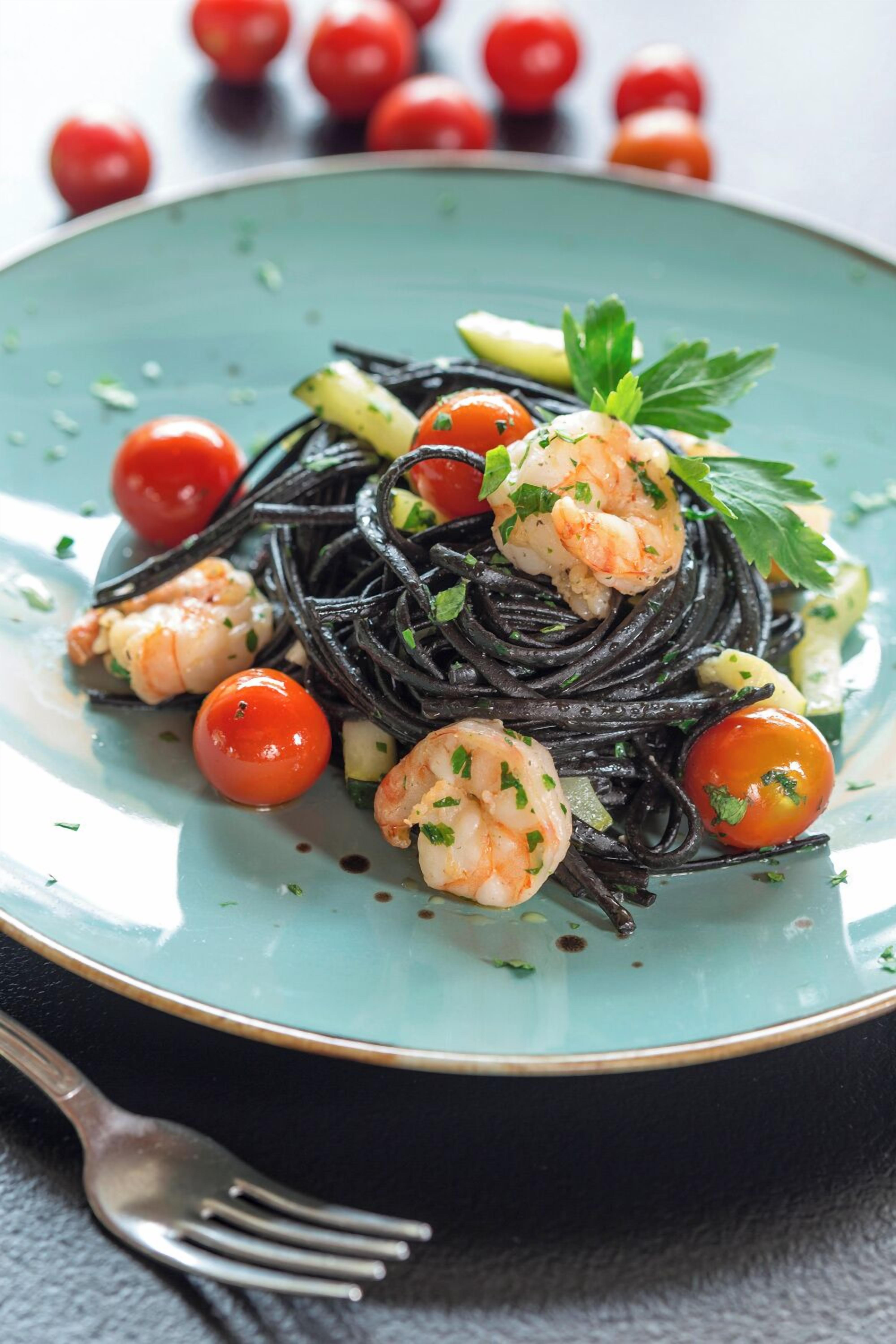 A plate of black pasta with shrimp and cherry tomatoes, garnished with parsley.