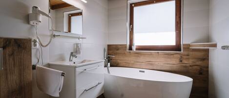 A modern bathroom with a freestanding bathtub, a vanity with a mirror, and a towel hanging on a rack.