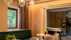 A modern interior with a wooden ceiling, a green sofa, round tables, and chairs. - Hotel Post Fusch (Fusch an der Grossglocknerstrasse)