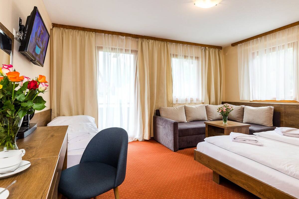 A hotel room with a bed, a sofa, a desk with a chair, a TV, and a window with curtains.