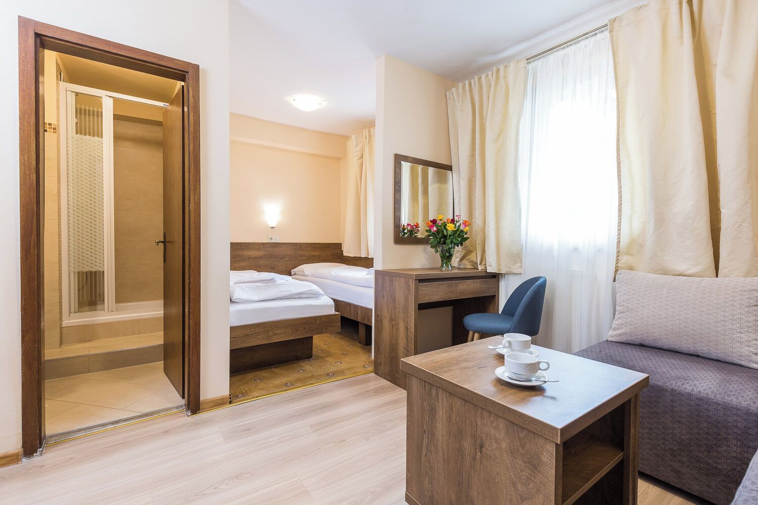 Una habitación de hotel con un escritorio de madera, un sofá, una cama y una zona de ducha.