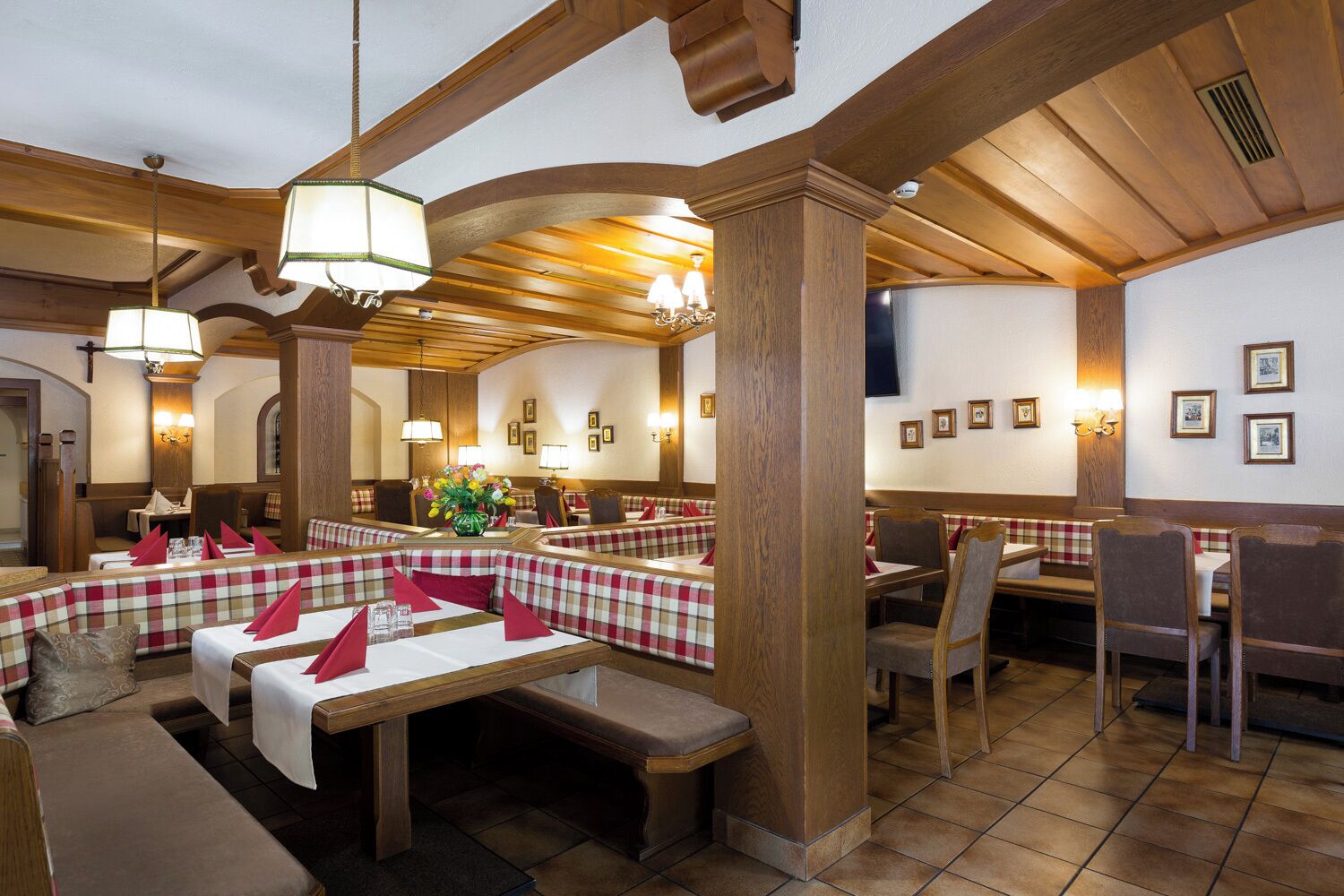 Ein Restaurant mit Holzbalken, karierten Sitzecken und Tischen mit roten Servietten.