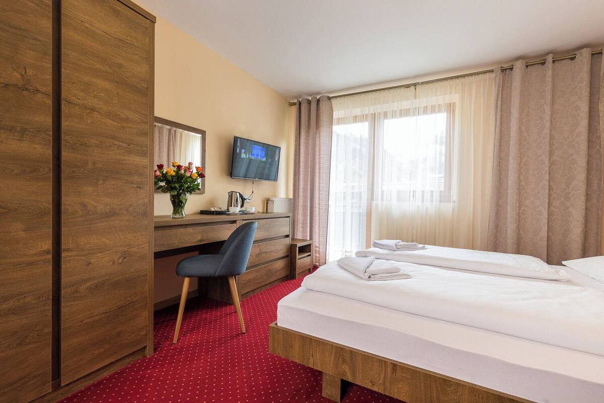 A hotel room with a bed, a desk with a chair, a television, and a window with curtains.