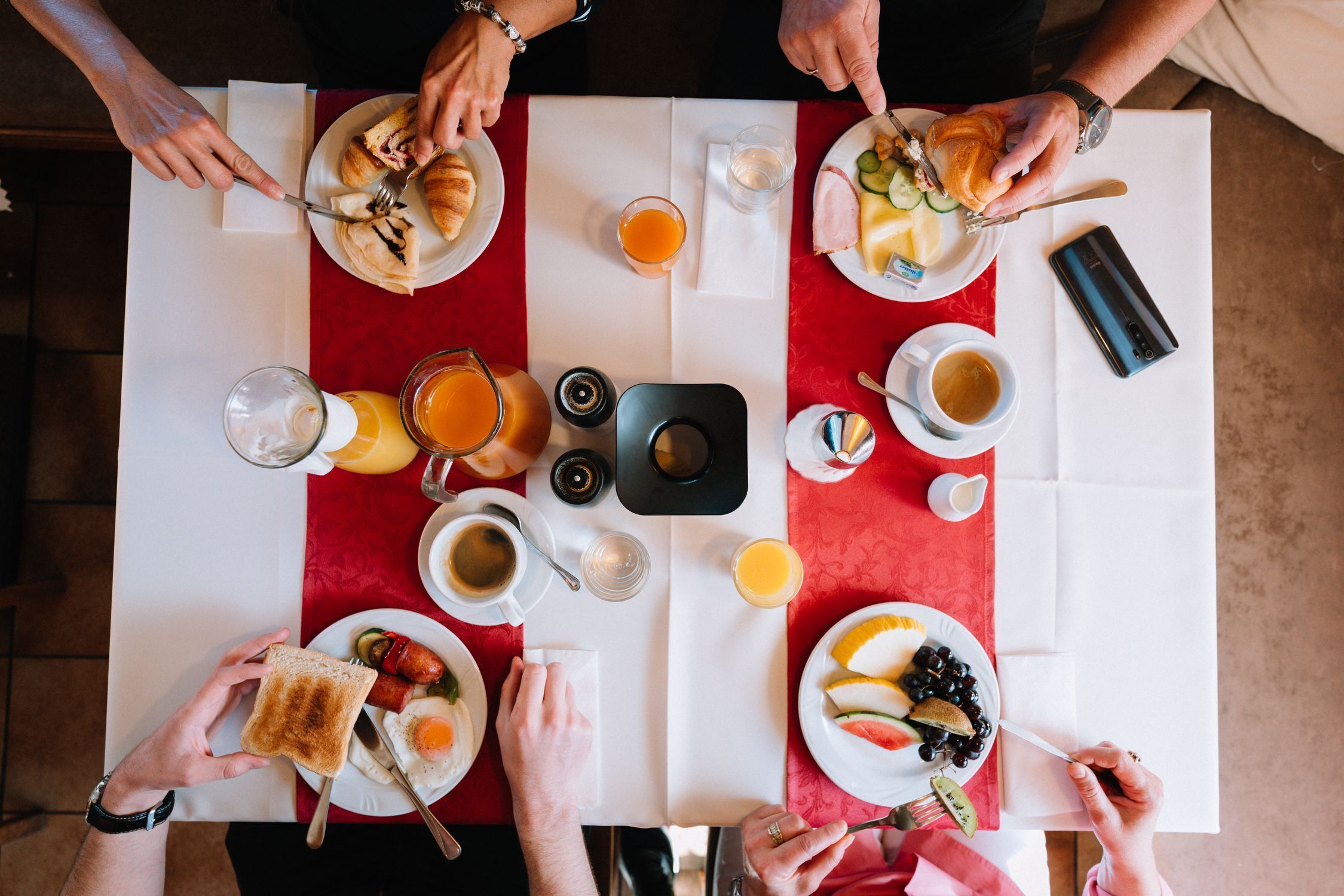 A breakfast setting with multiple plates of food, cups of coffee, and a smartphone on the table.