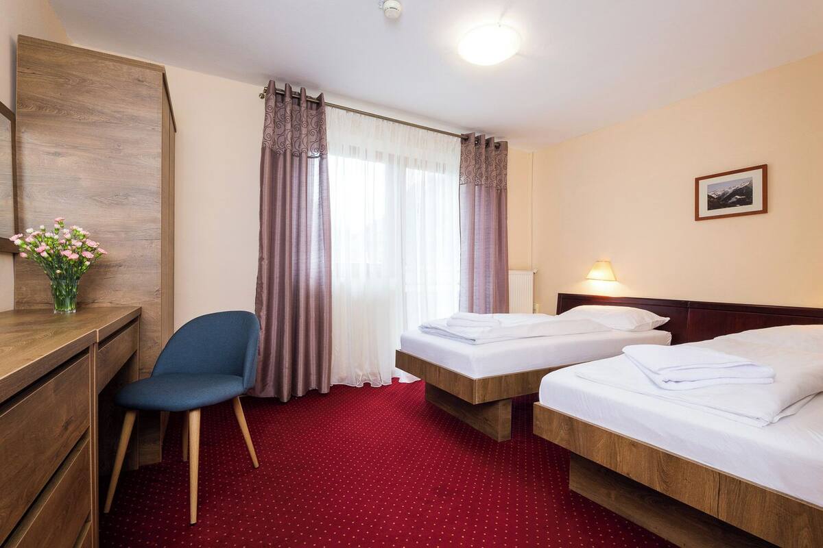 A hotel room with two beds, a desk, a chair, and a window with curtains.