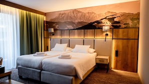 A hotel room with a large bed, two bedside tables, a wooden headboard, and a mountain landscape mural on the wall. - Hotel Post Fusch (Fusch an der Grossglocknerstrasse)