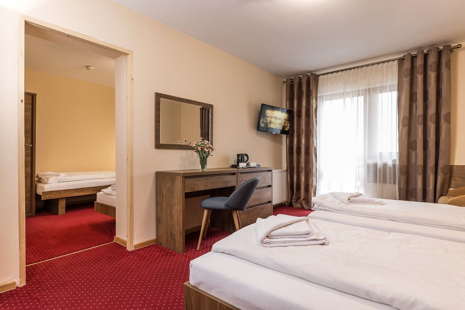 A hotel room with two beds, a desk with a chair, a television, and a window with curtains.