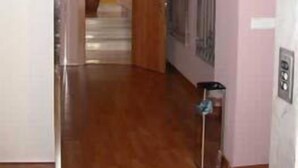 Un pasillo con suelo de madera, una puerta con ventanal y una pared con un cartel.