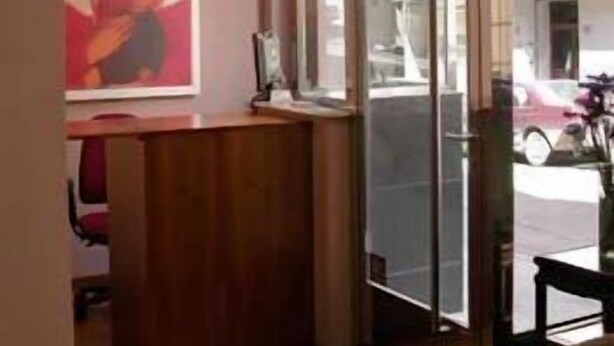 Un área de recepción con un escritorio de madera, una obra de arte enmarcada en la pared y vista a la calle a través de una puerta de cristal.