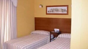 Habitación de hotel con dos camas, cabecero de madera, un cuadro en la pared y una mesita de noche con lámpara.