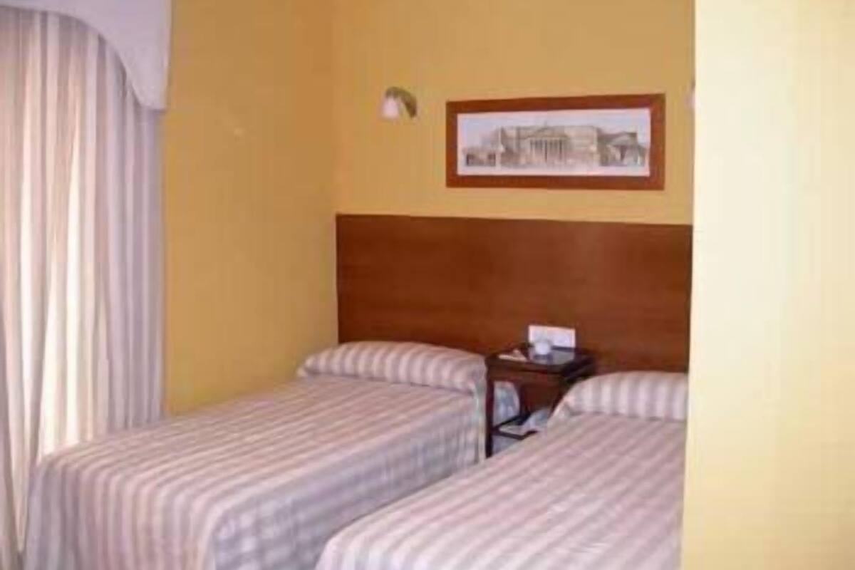 A hotel room with two beds, a wooden headboard, a framed picture on the wall, and a nightstand with a lamp.